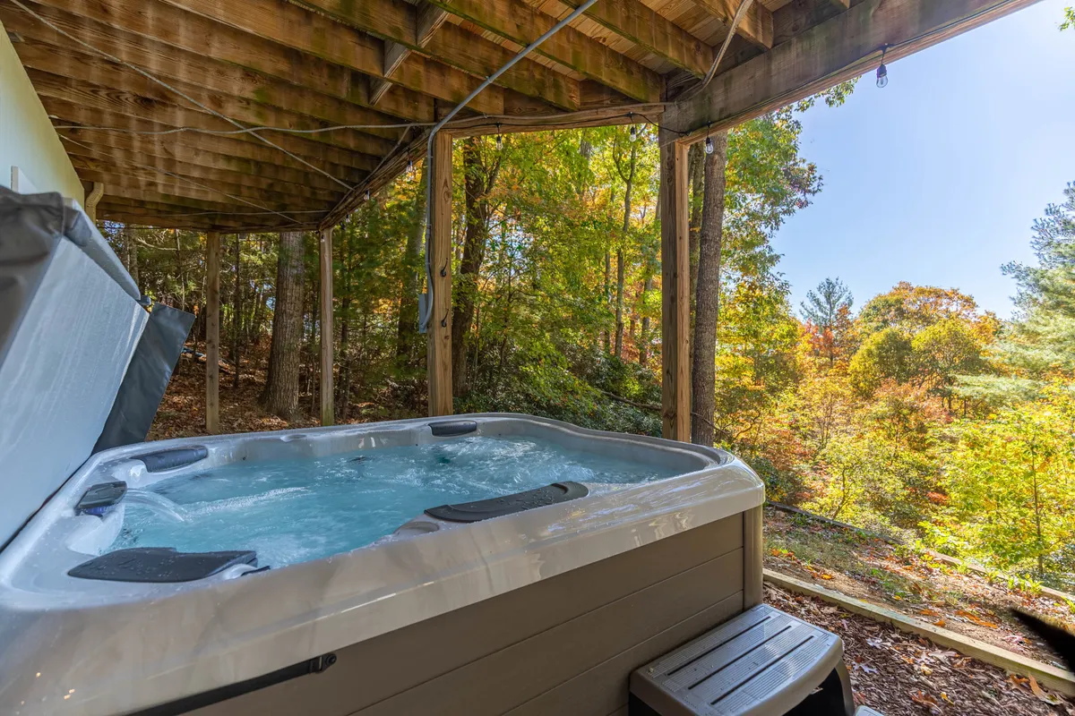 An exterior view of the luxurious six-person hot tub nestled among trees, with mountains visible in the background. The scene exudes tranquility and luxury, promising relaxation under the open sky.