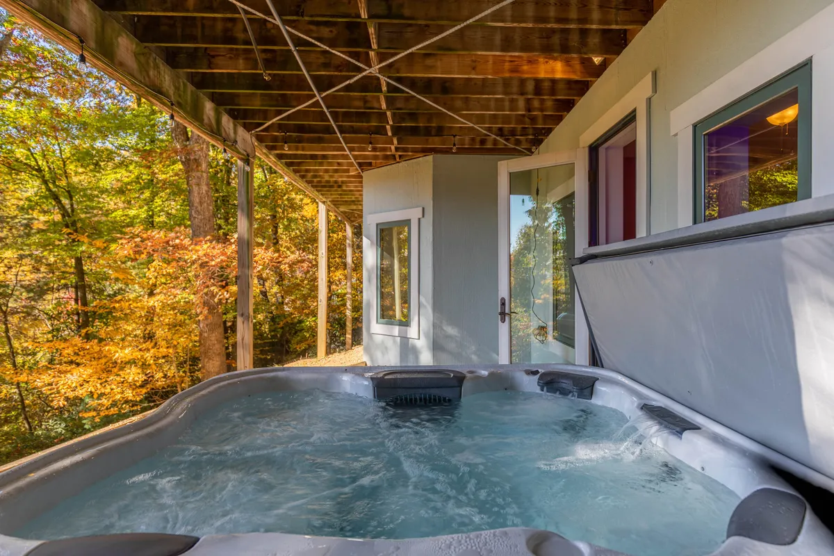 This exterior image showcases a hot tub set among surrounding trees, with a doorway hinting at the connection between indoor comfort and outdoor adventure. The scene exudes tranquility and offers a glimpse of the natural setting surrounding Tobey’s Den, ideal for guests and their pets to unwind after outdoor activities.