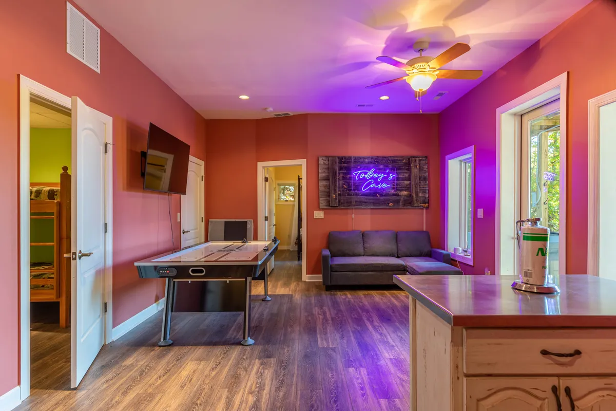 A vibrant game room scene shows friends engaged in a lively game of air hockey, with a neon sign adding playful ambiance. A comfy sofa sits nearby, inviting relaxation or spectating.