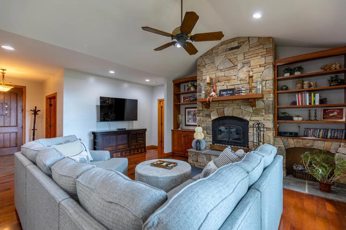 A welcoming living area centered around a stone fireplace with a distinctive mantle, a comfortable sofa, wooden shelves, and a TV. This setting is ideal for sharing stories, movie nights, or relaxing by the fire.