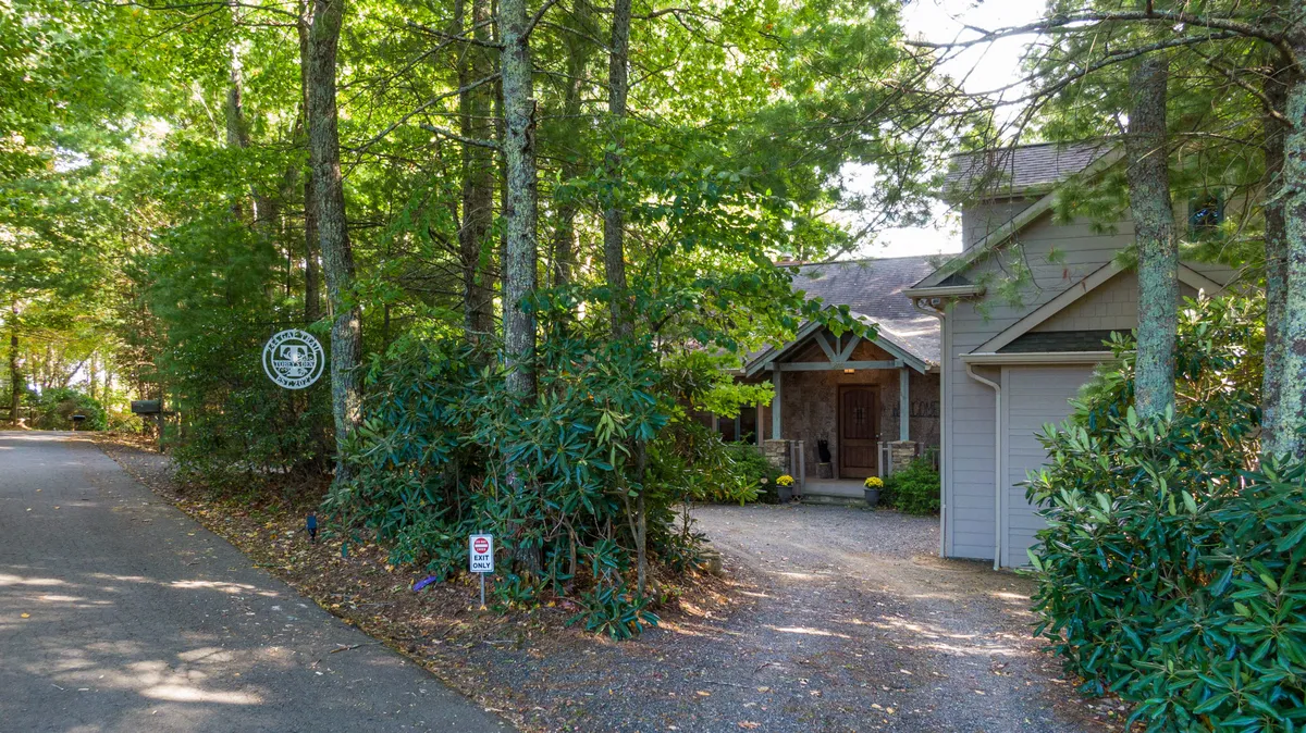 This image shows the front entrance of the house surrounded by lush greenery and a driveway leading up to the home. The scene evokes a sense of arrival and connection to nature, hinting at the proximity to local trails and outdoor adventures.