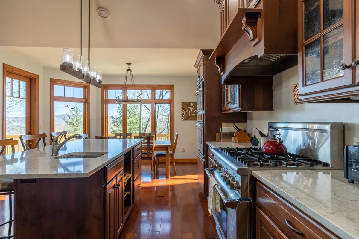 A bright, open kitchen and dining space with a kitchen island, stainless steel stove, large windows, and wooden dining chairs. The room feels welcoming and functional, with easy-to-clean surfaces that are practical for guests traveling with pets. The windows further connect the interior to the outside environment.