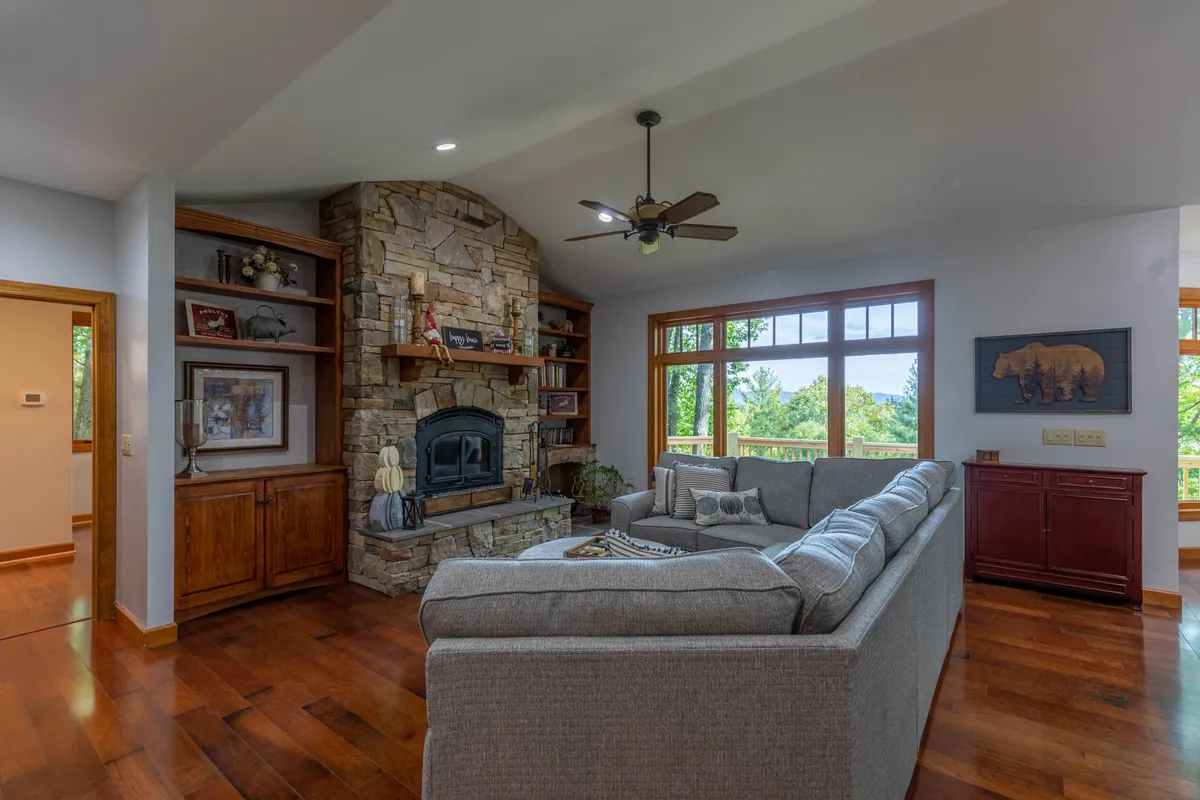 A comfortable living area centered around a beautiful stone fireplace, with plush seating positioned to encourage conversation and relaxation. Generous windows let in natural light and offer glimpses of the outdoors.