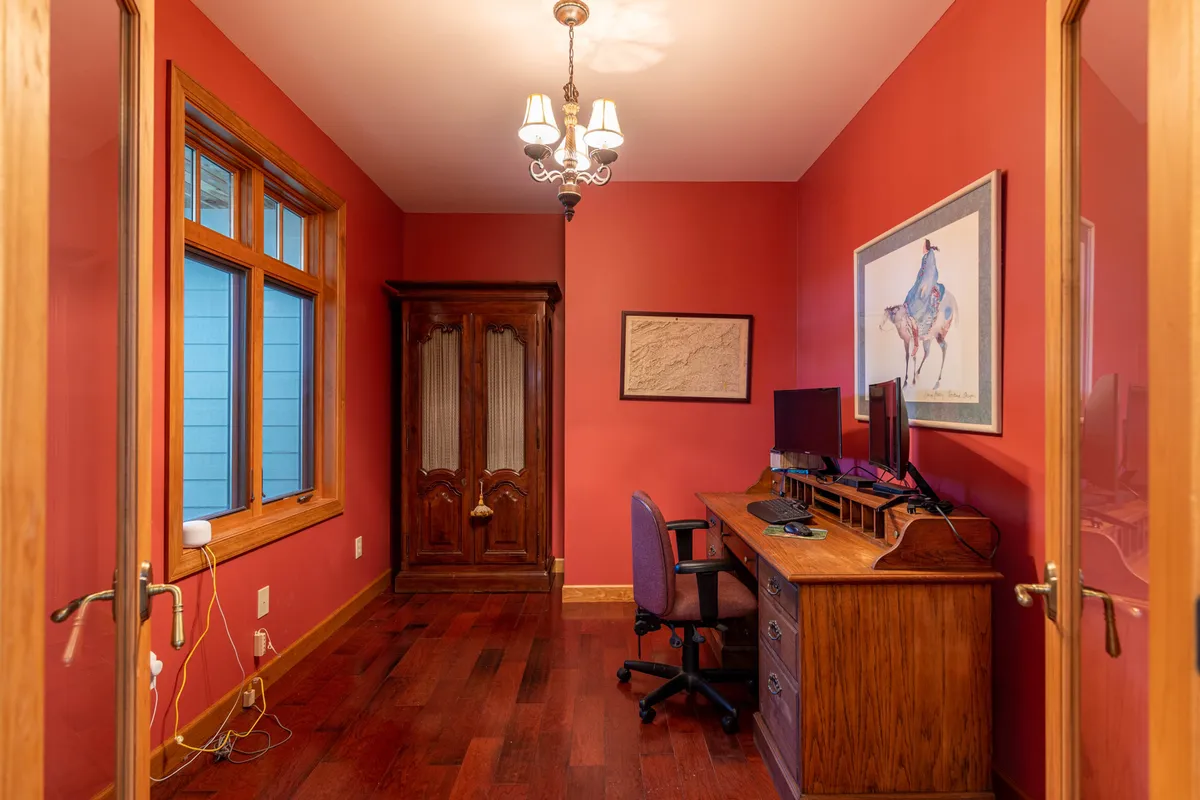 A dedicated office area with a wooden desk, computer setup, ornate cabinet, artwork, and an elegant chandelier. The mood is productive and serene, offering a comfortable spot for remote work or creative inspiration.