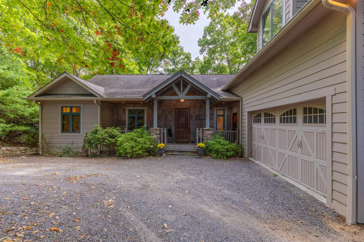 The hero image showcases the welcoming front entrance of Tobey's Den, surrounded by lush landscaping and featuring a spacious driveway with a garage. The inviting porch hints at relaxing mornings with coffee, while the ample outdoor space suggests gatherings and family barbecues in a tranquil mountain setting.